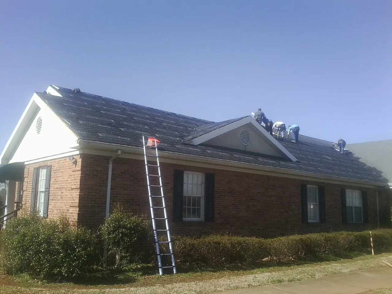 Crew tearing shingles off a brick ranch roof with a ladder set — Emergency Roof Repair work by our crew in Pawtucket