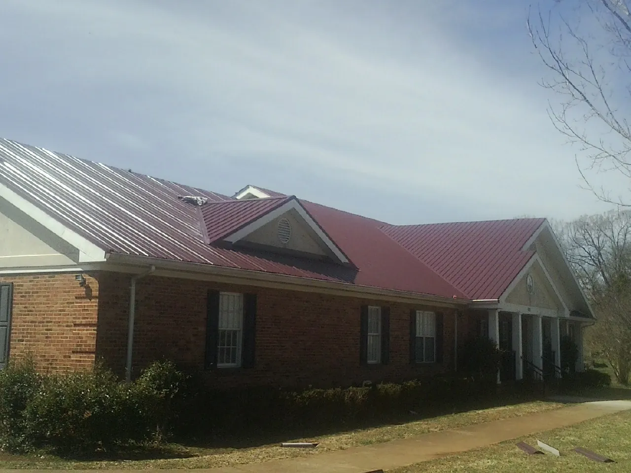 Red metal roof with gabled entries on a long brick building, from a Hail Damage Roof Repair job in Pawtucket