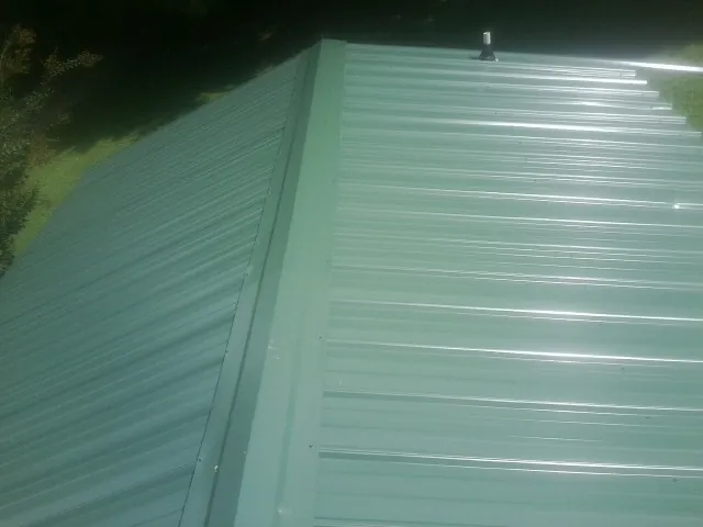 New green metal panels meeting at the ridge of a roof — Flat Roof Repair work by our crew in Pawtucket