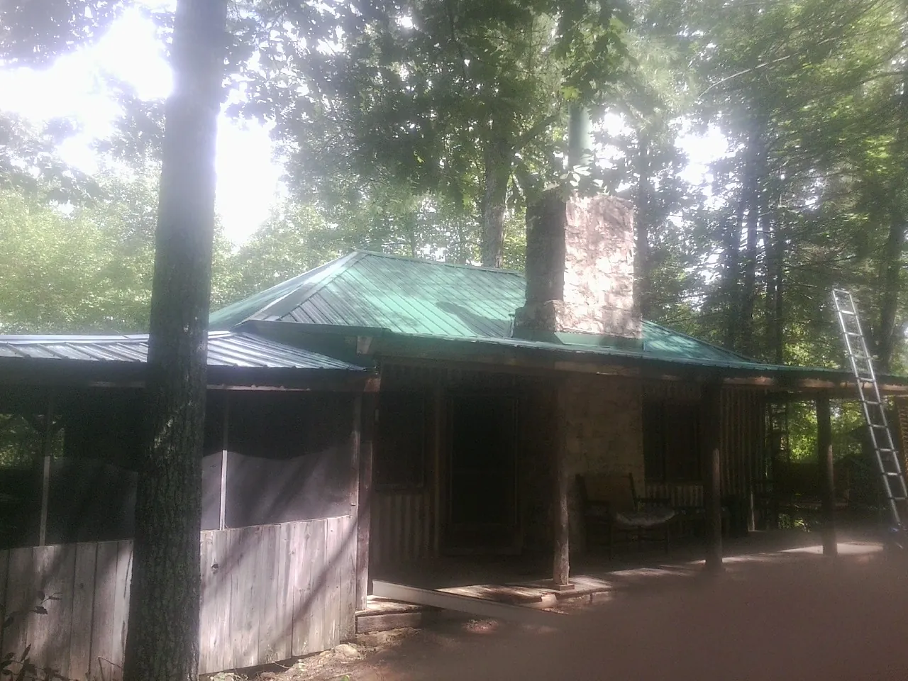 Green metal roof and stone chimney above a log cabin porch in Pawtucket