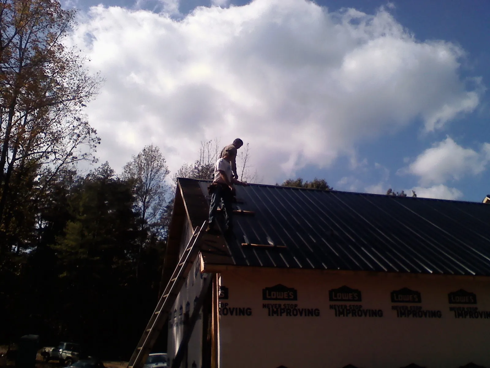 Roofer fastening dark metal panels high against a cloudy sky, from a Roof Inspection job in Pawtucket